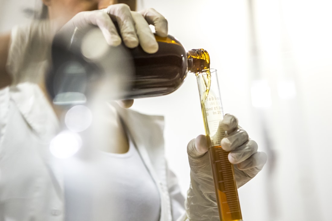 Technician in gloves pouring an amber liquid into a graduated cylinder